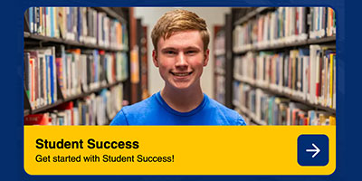 Male student smiles for the camera in the library stacks
