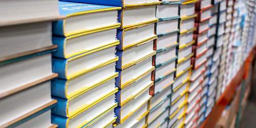 Multiple stacks of textbooks on a shelf.