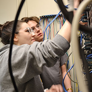 Two computer networking students attaching cables to a switch.