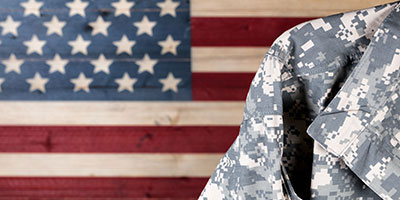 A closeup of a soldier in a camo jacket standing in front of the American flag.