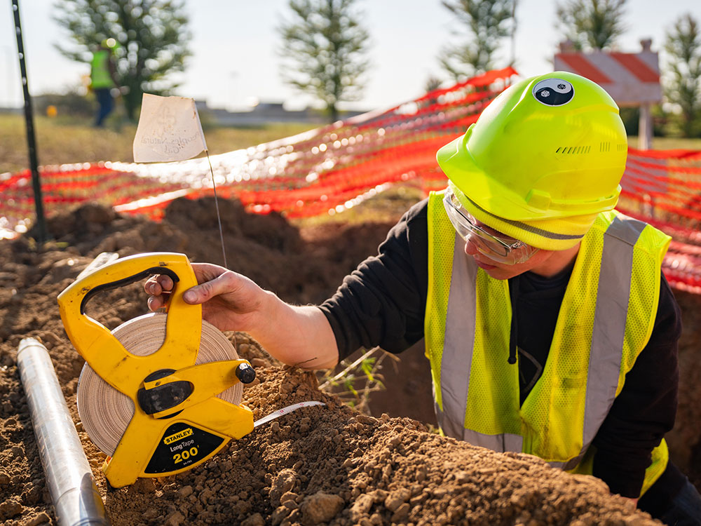 Student measuring large hole dug in ground