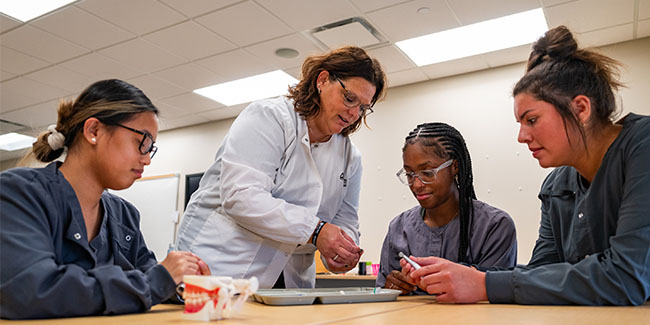 Three dental assisting students work at a table with their instructor.