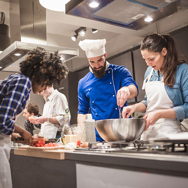 Male chef teaches adults how to cook in large kitchen