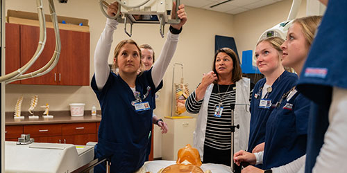 A rad tech student positions an x-ray machine in front of a mannequin.